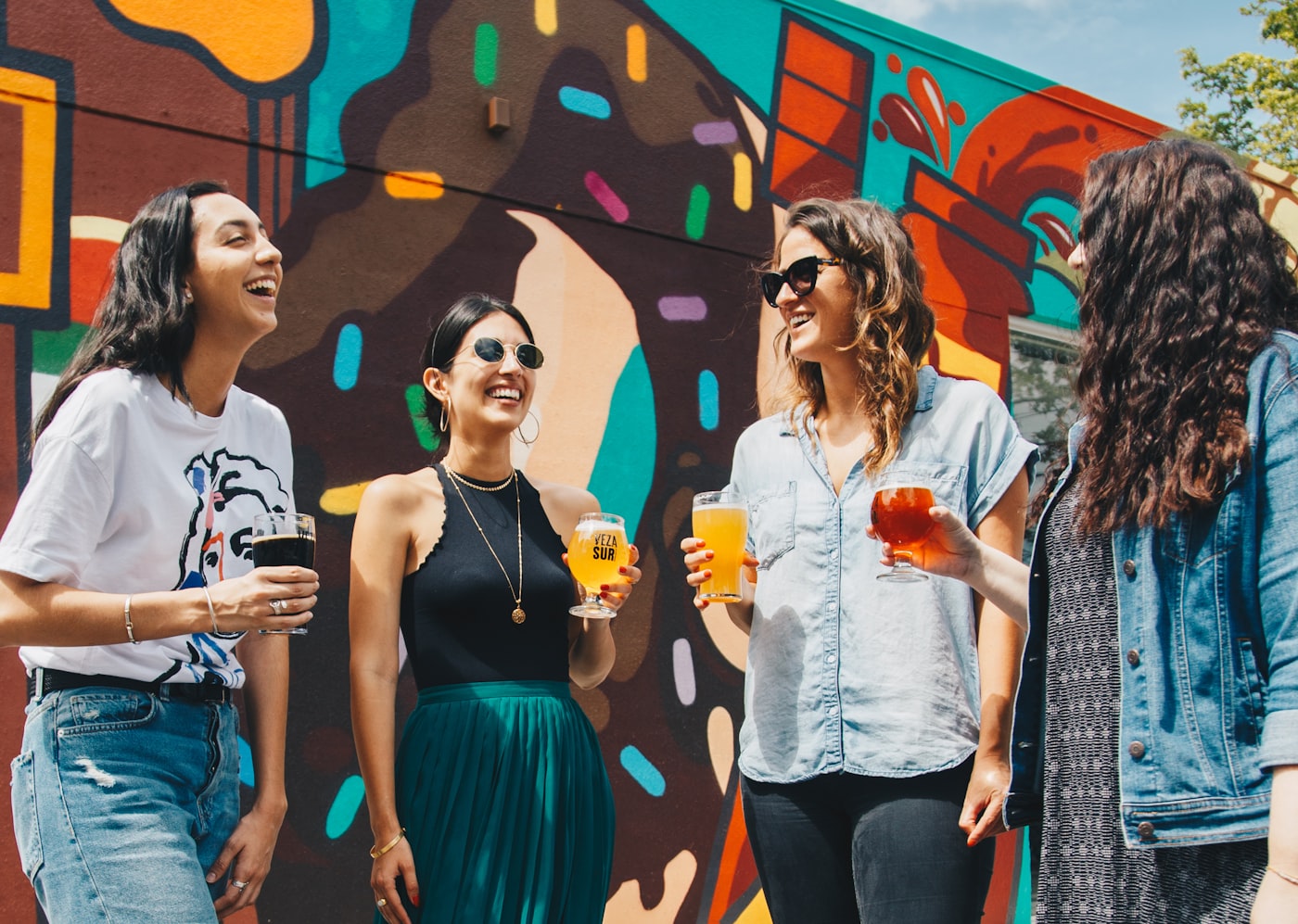 Empat perempuan ketawa bareng di depan mural warna-warni